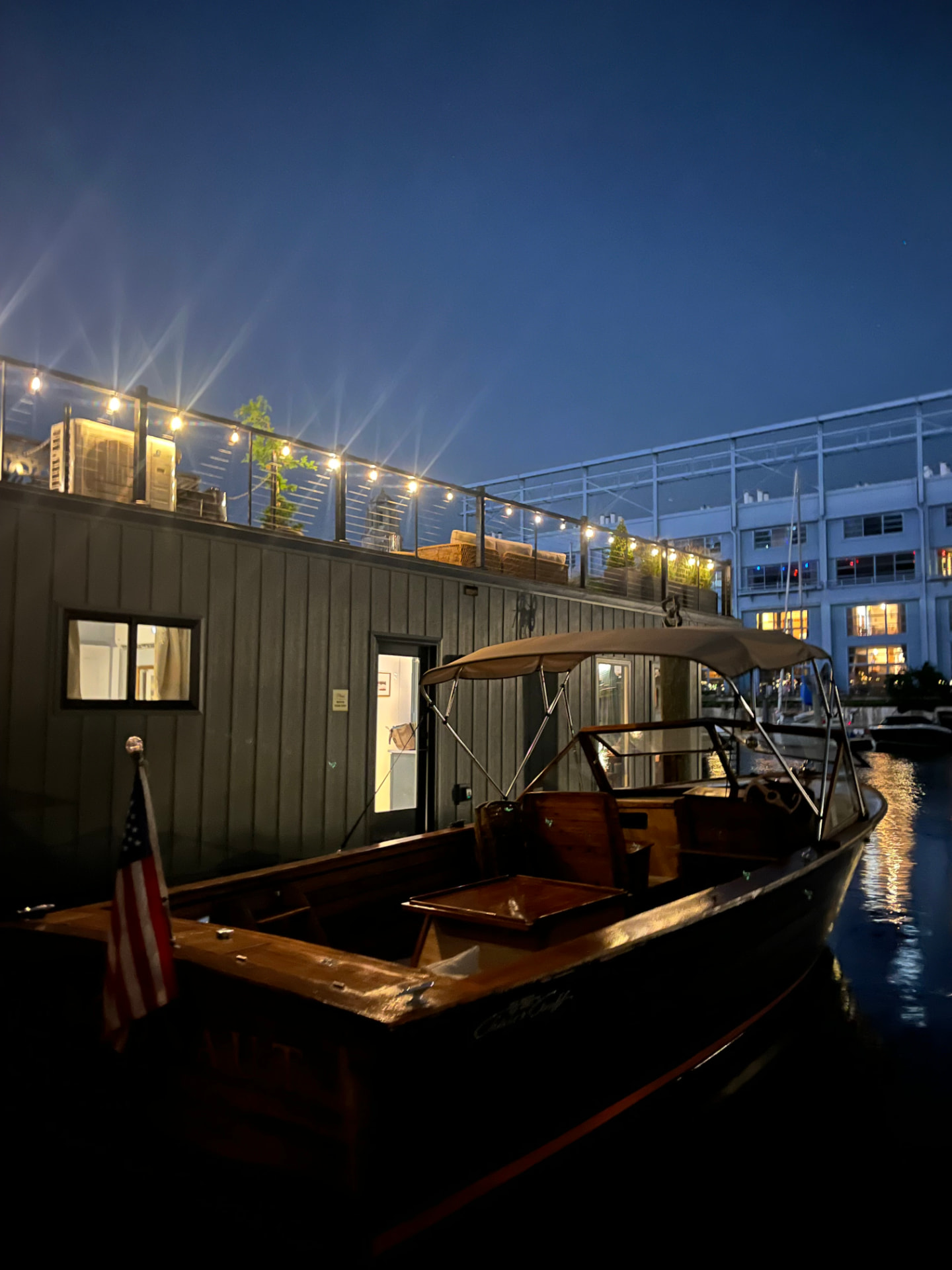 The houseboat at night in the marina, roof deck glowing under string lights