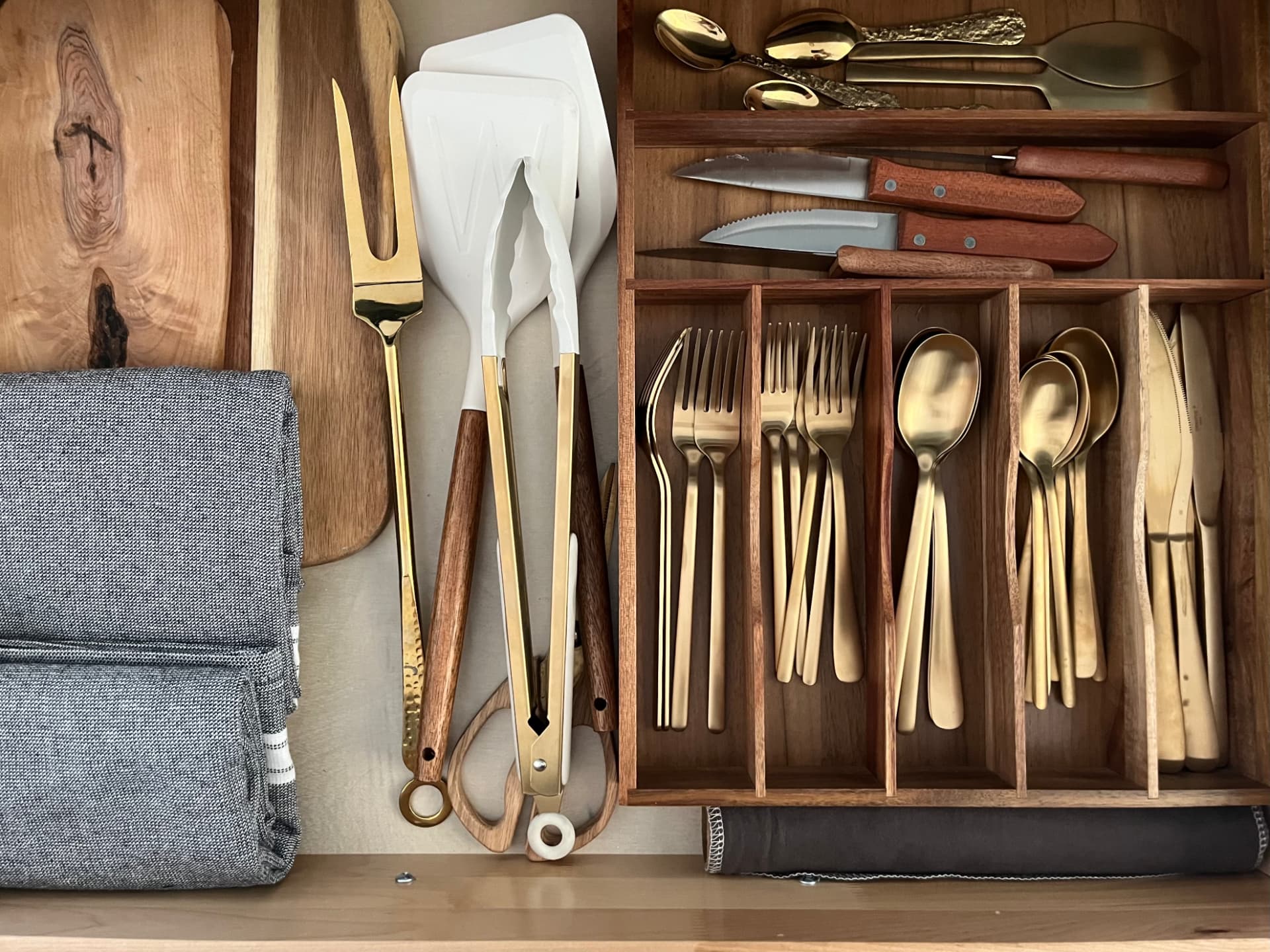 An open kitchen drawer with flatware and boards neatly arranged